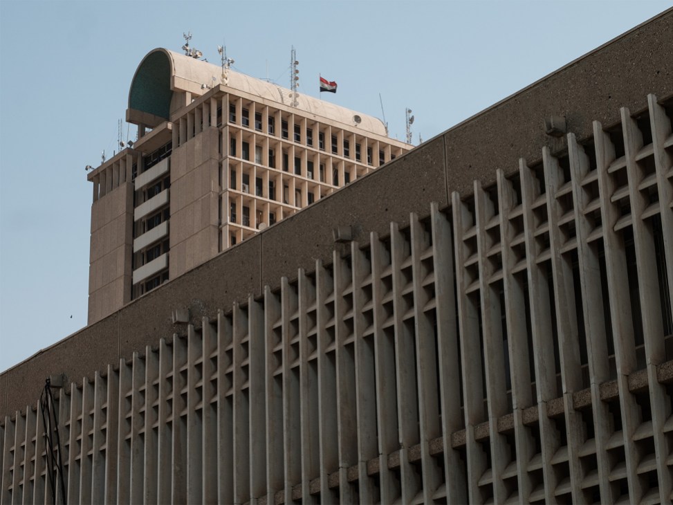 Walter Gropius's Faculty Office Tower at University of Baghdad, a tan concrete modernist high-rise with regular window grid and communications antenna, flying an Iraqi flag.