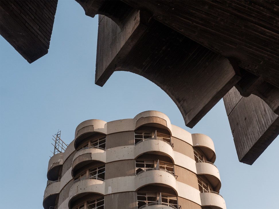 Upward view of the 1962 Ten Fils Building showing curved concrete balconies beneath dark modernist concrete overpass structure