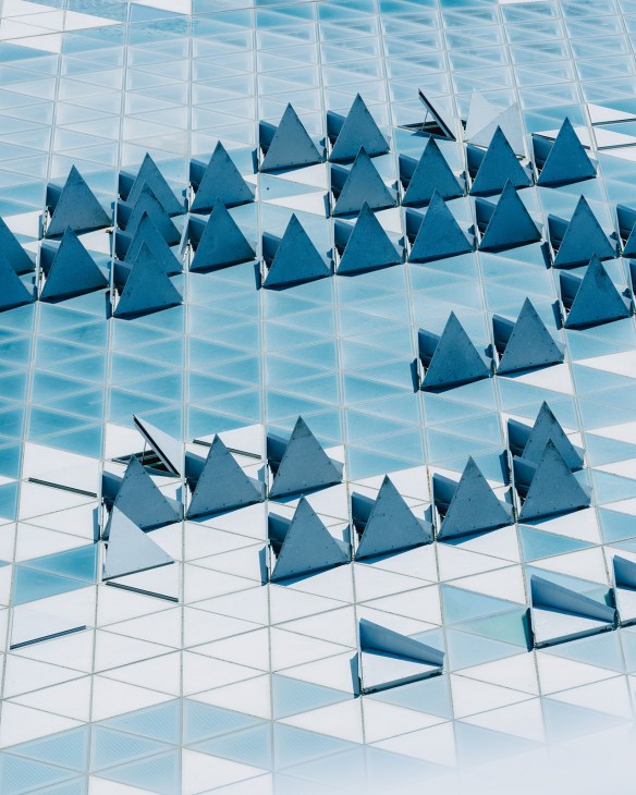 Blue pyramid-shaped architectural elements mounted on a white latticed glass ceiling at La Platine exhibition space.