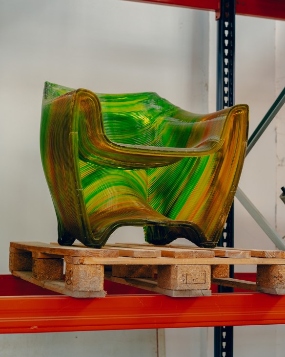 Green and orange 3D-printed chair by Post Industrial Crafts displayed on wooden pallet.