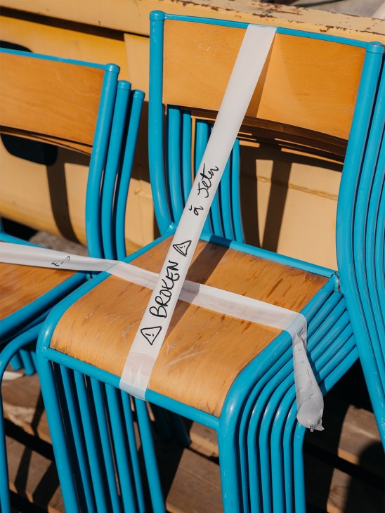 Blue chairs with woven rush seats bound with white tape labeled 'Broken' and repair marks.