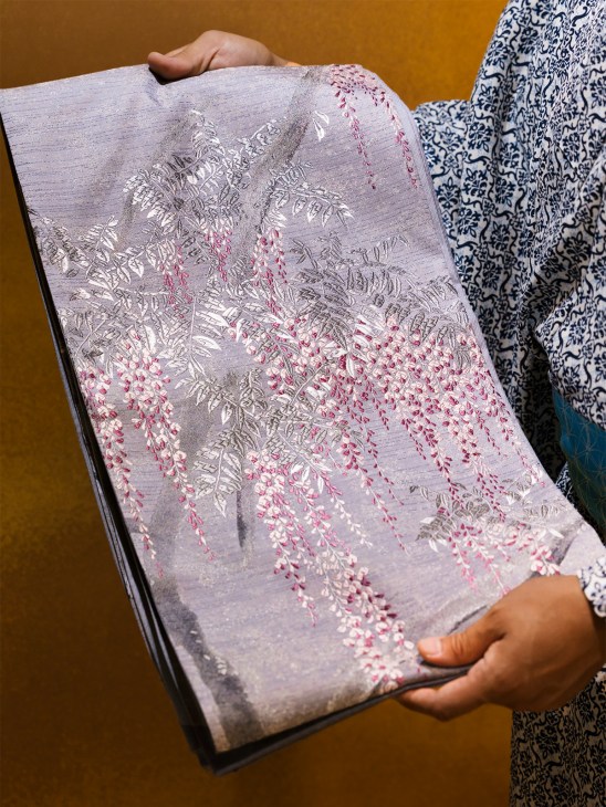 Person holding a lavender kimono sash with white and pink floral embroidery by Rokumonjiya.