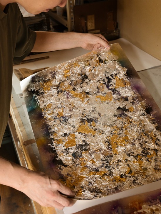 Hands holding metallic foil paper with gold and silver fragments used in Nishijin textile weaving.