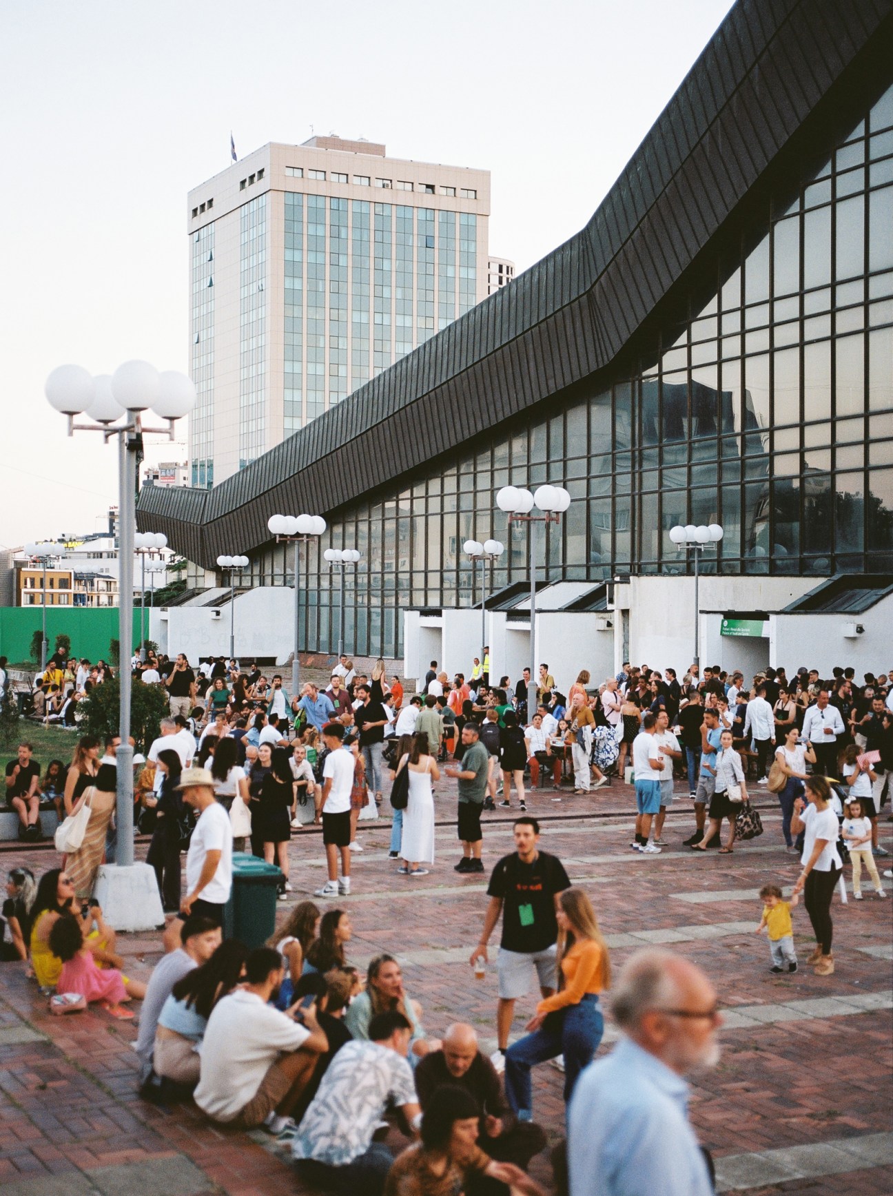Large crowd gathered in front of modern glass building with curved architecture during evening event