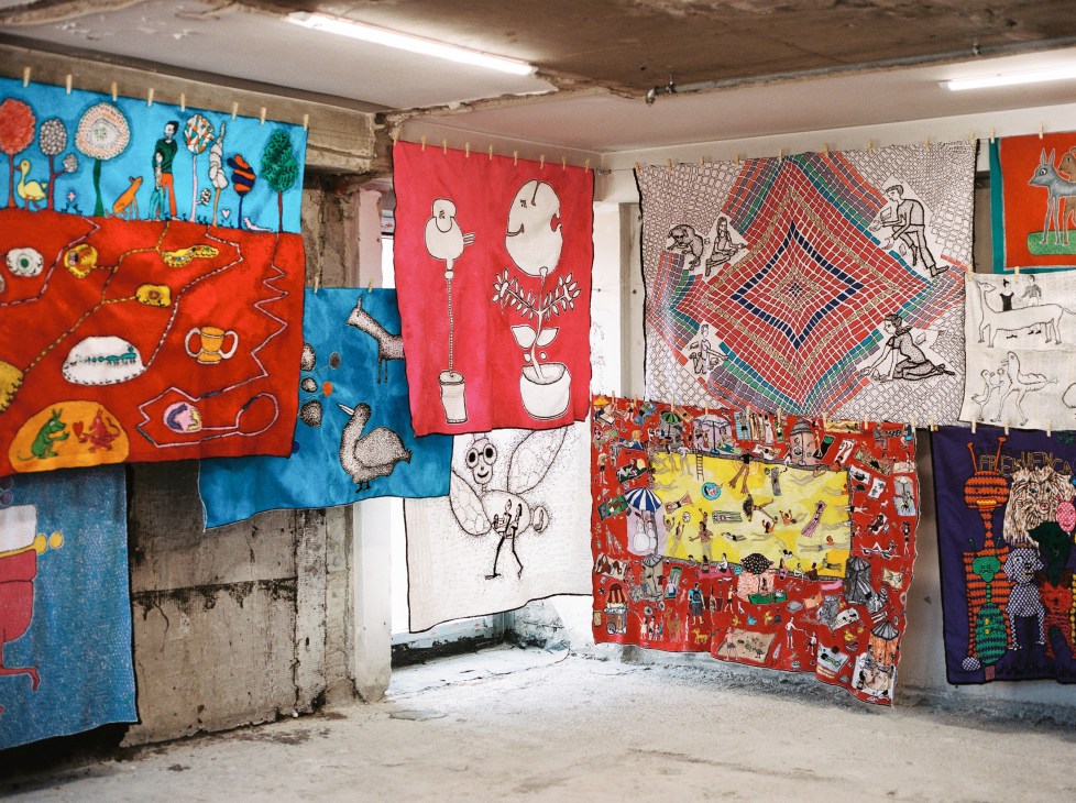 Colorful tapestries with geometric patterns and folk motifs hanging on clotheslines in a basement space