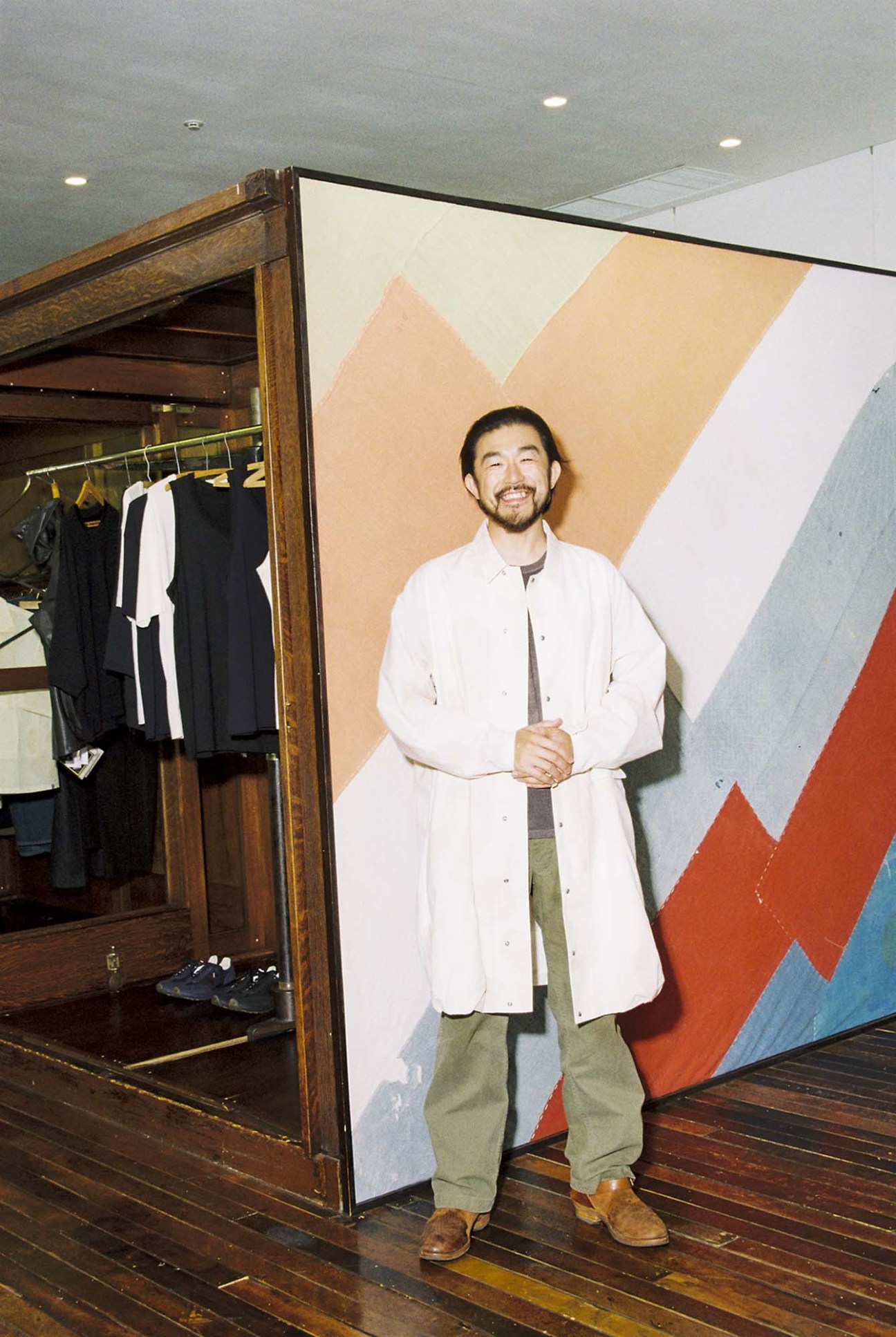 Man in white coat standing in front of geometric wall art in a studio setting.