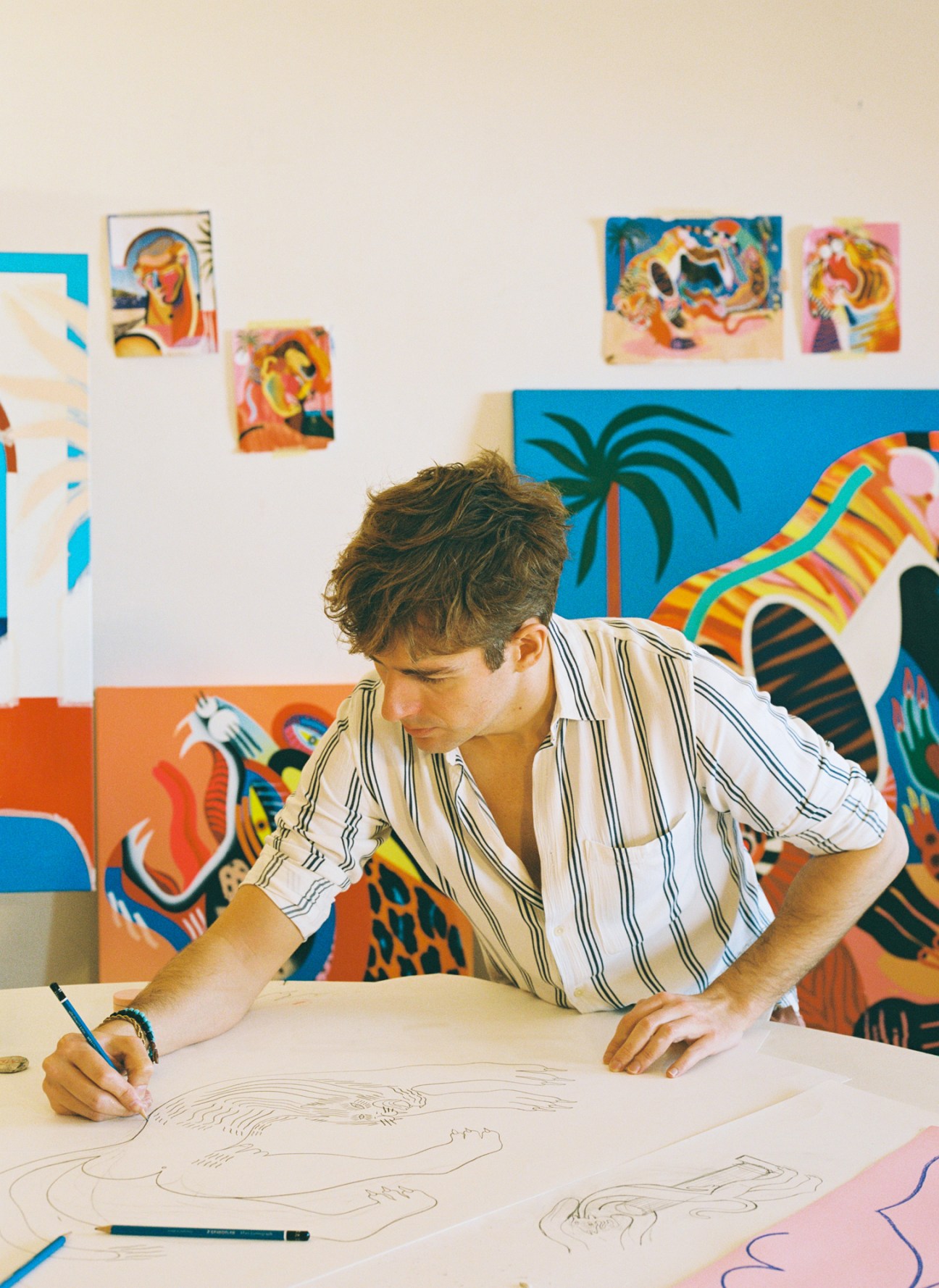 Albert Madaula drawing at a table surrounded by colorful artwork in his Barcelona studio