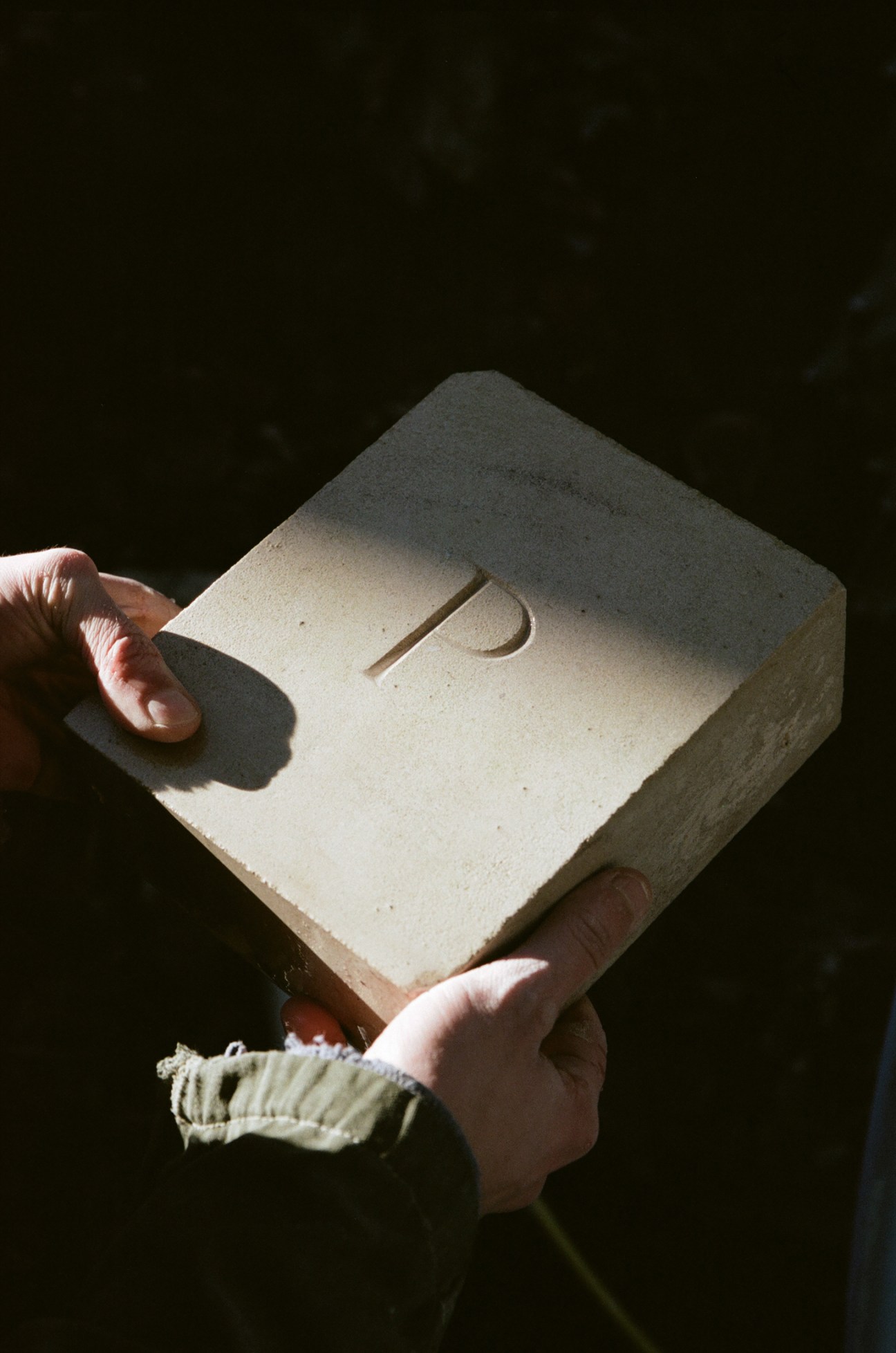 Hands holding a white stone block with carved letter P
