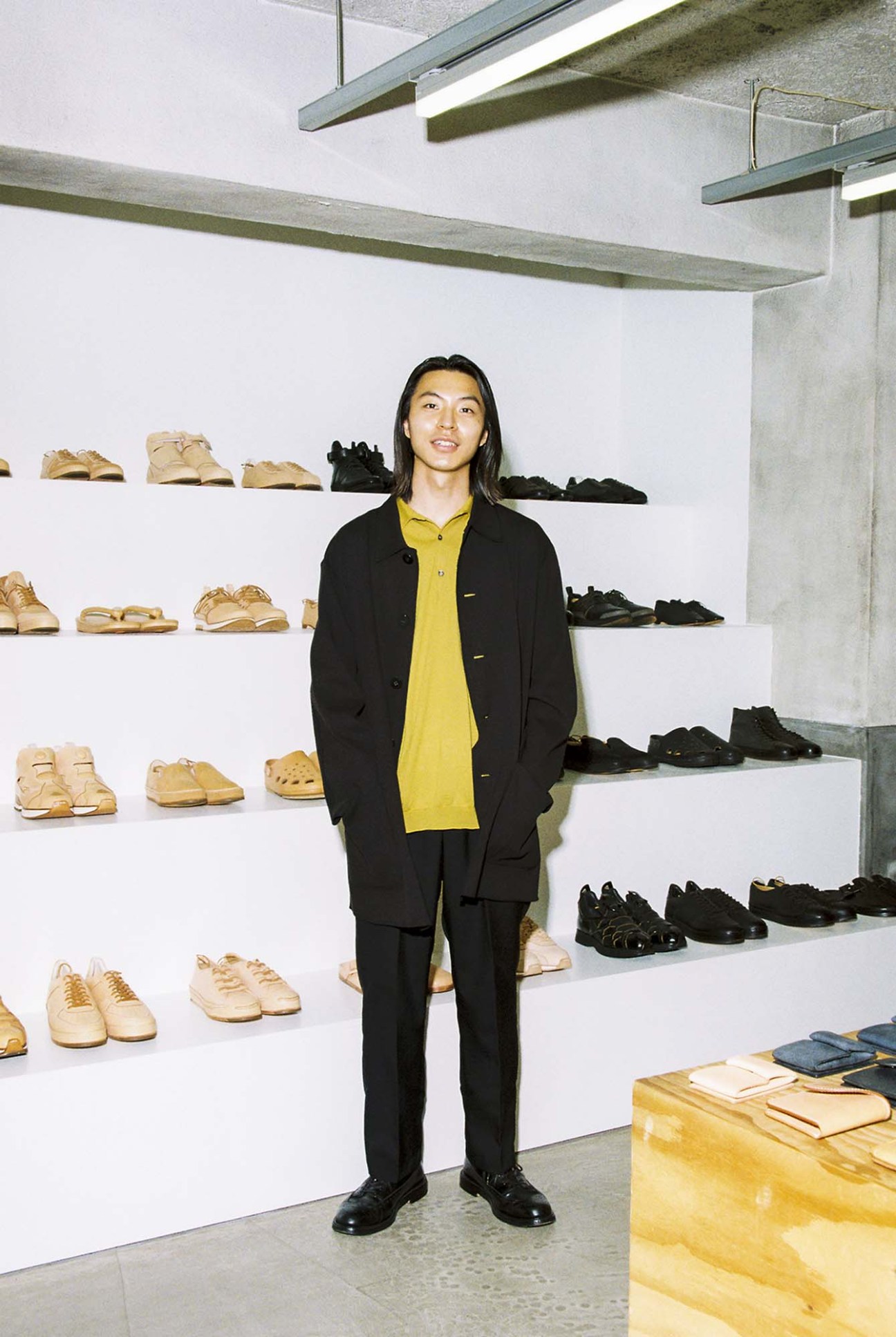 Toga Ikeda standing in Hender Scheme store with shoes displayed on shelves behind him
