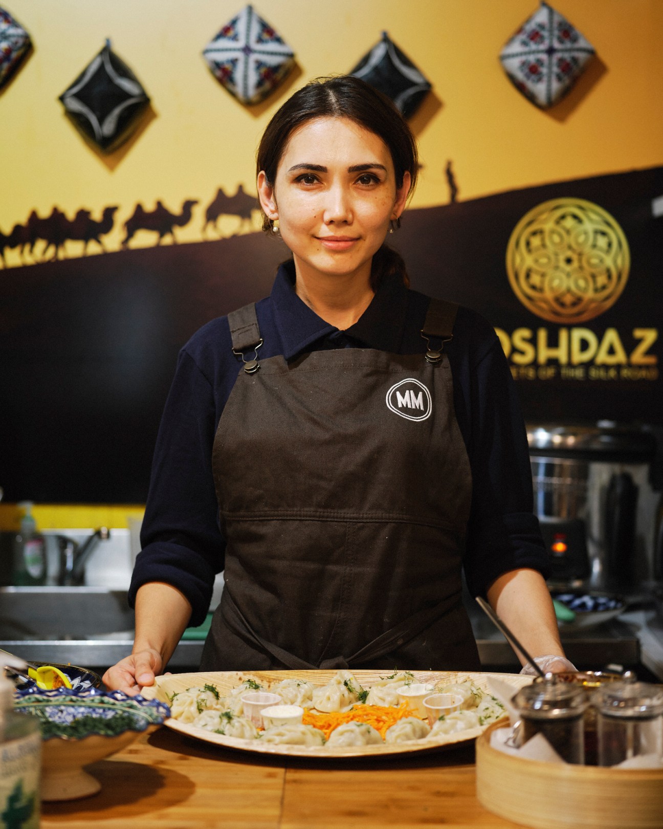 Woman in apron presenting food platter at Uzbek market stall