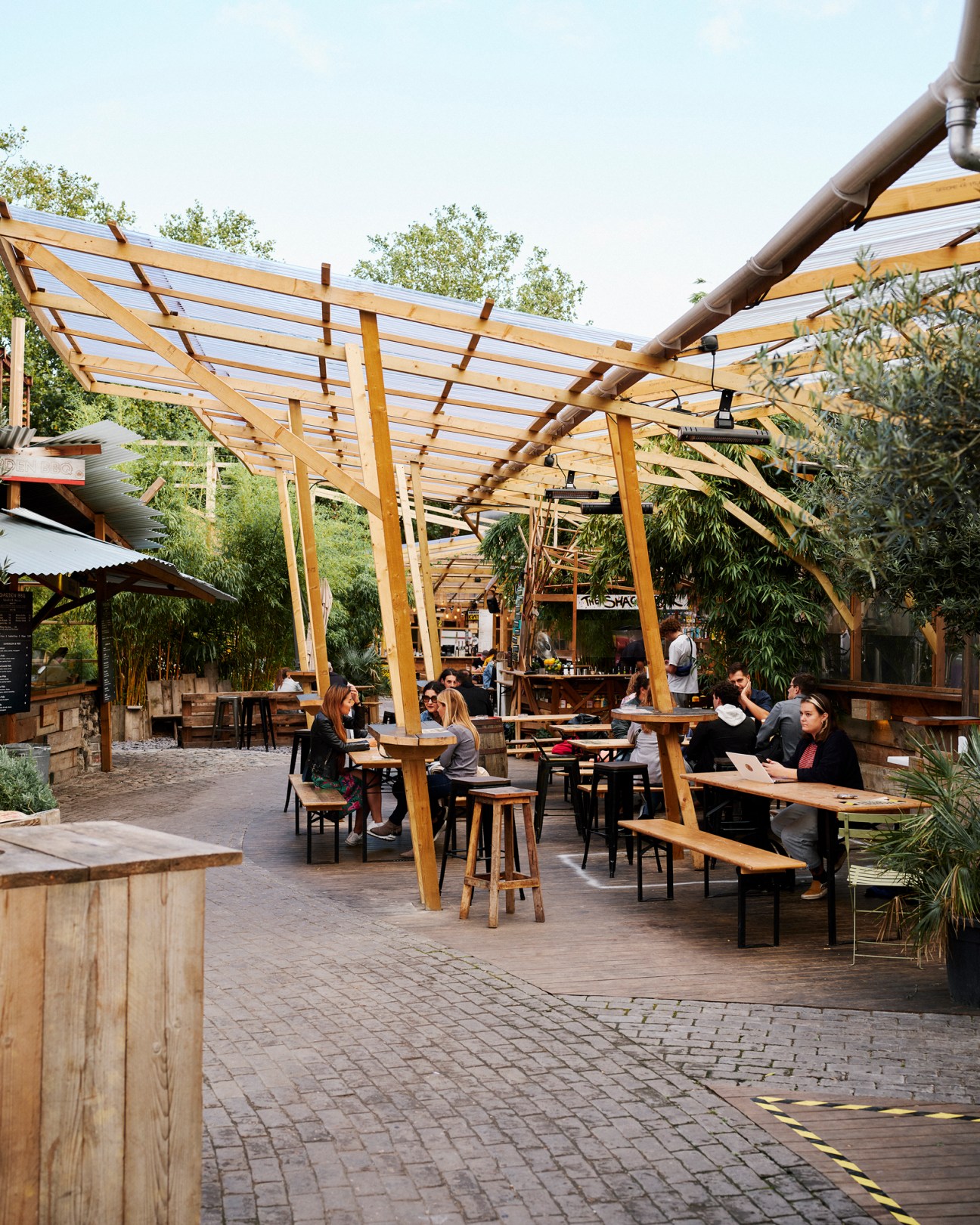 Outdoor dining area with wooden pergola structure, tables with customers, and lush greenery at Mercato Metropolitano