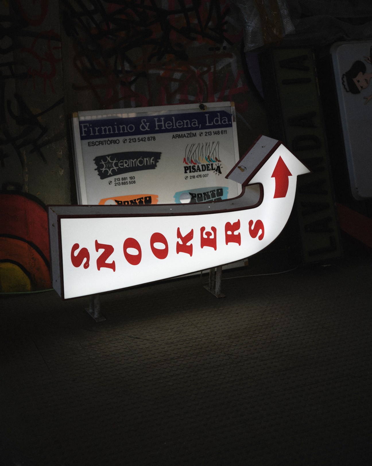 Vintage neon signs and business signage stored in a warehouse, including an arrow-shaped sign reading 'SNOOKERS'