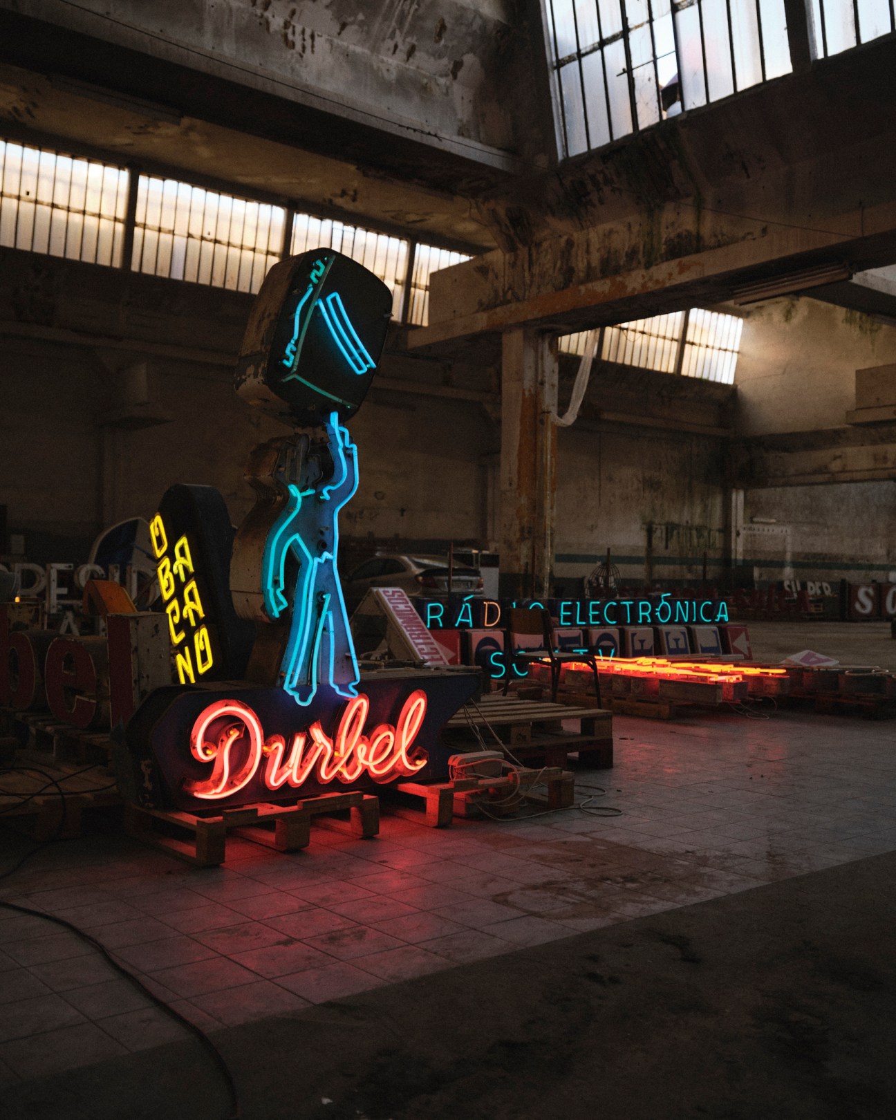 Illuminated neon signs displayed in a warehouse including blue figure holding briefcase and red Durbel script lettering