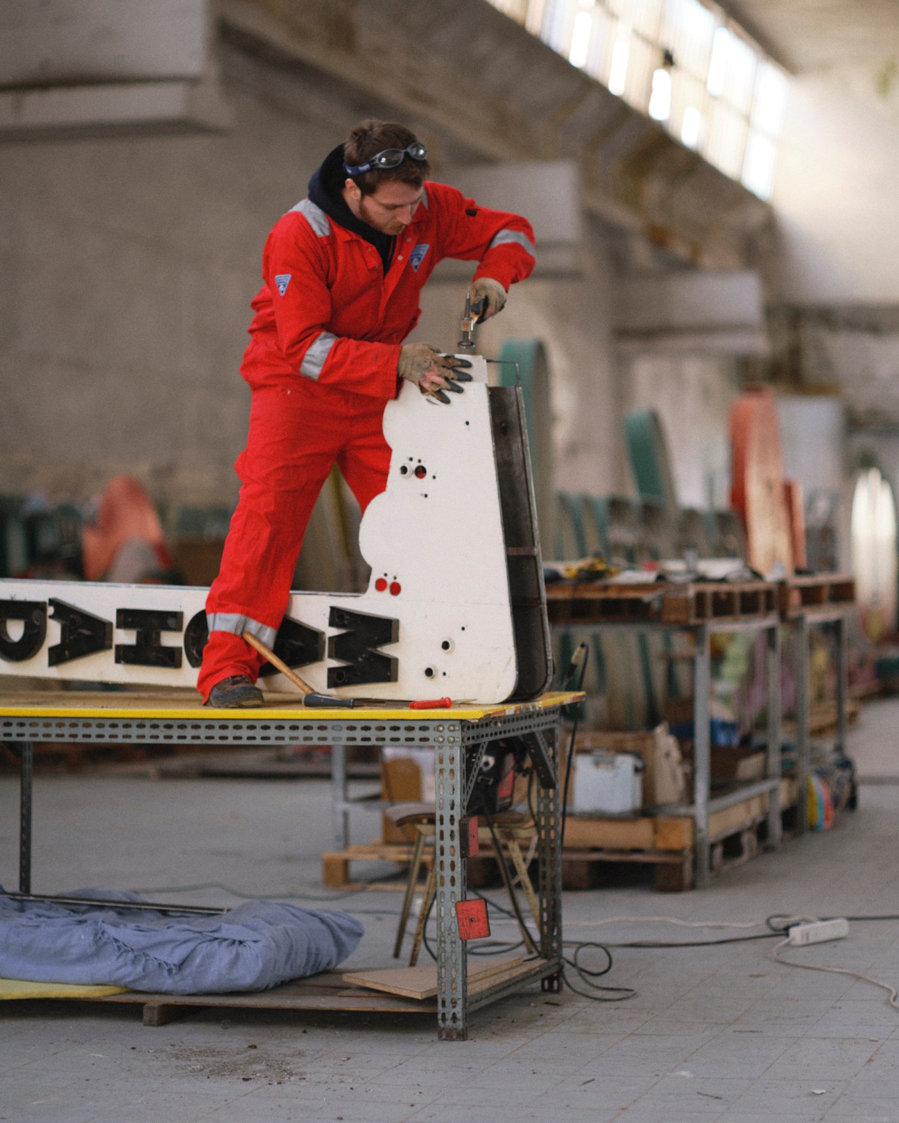 Person in red coveralls working on a white neon sign in a workshop