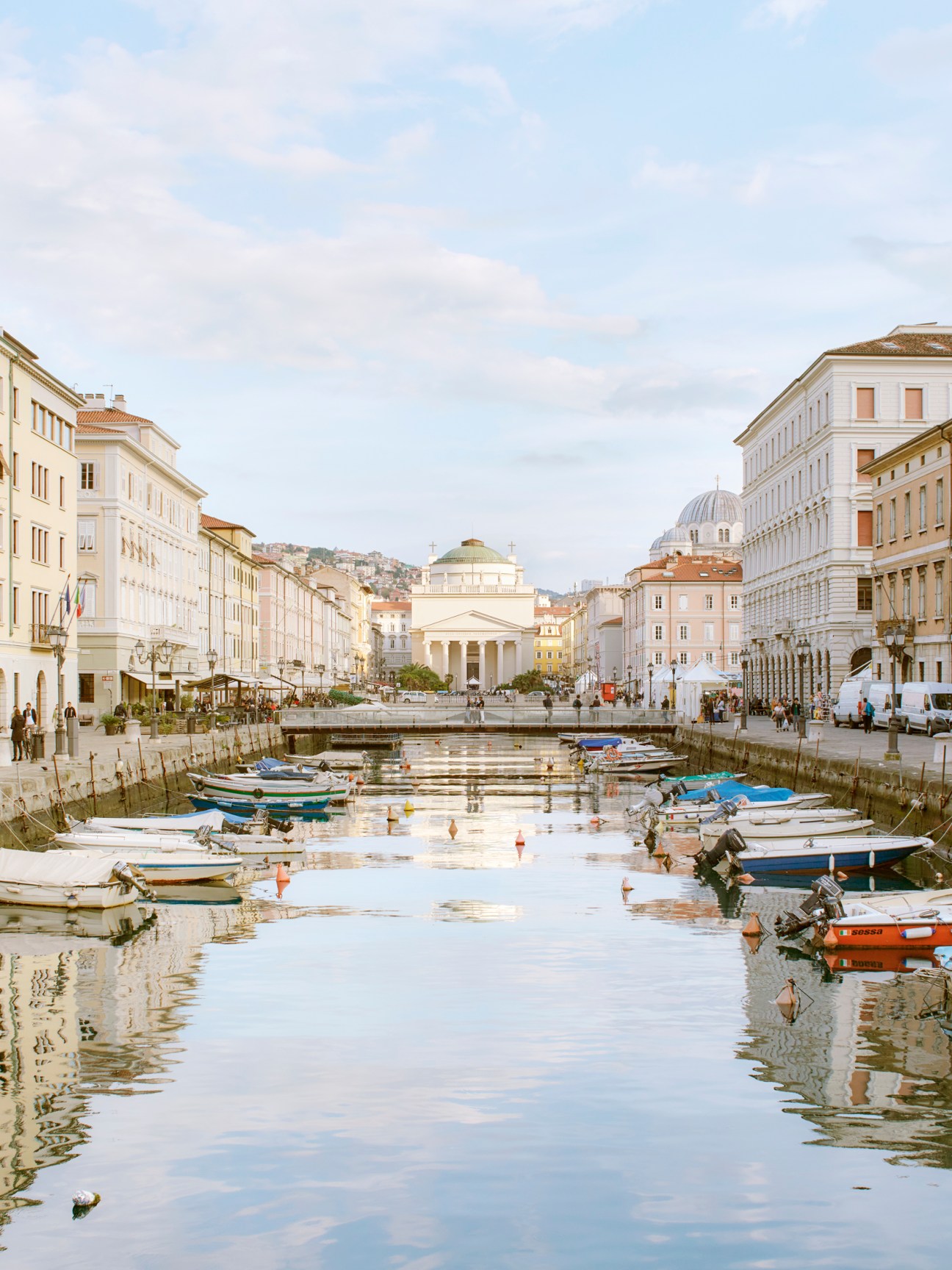 Trieste's canal with moored boats and neoclassical buildings reflected in calm water