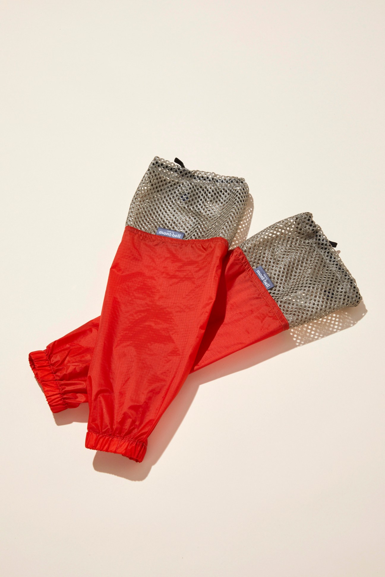 Montbell arm protectors with red fabric sleeves and grey mesh tops displayed against neutral background