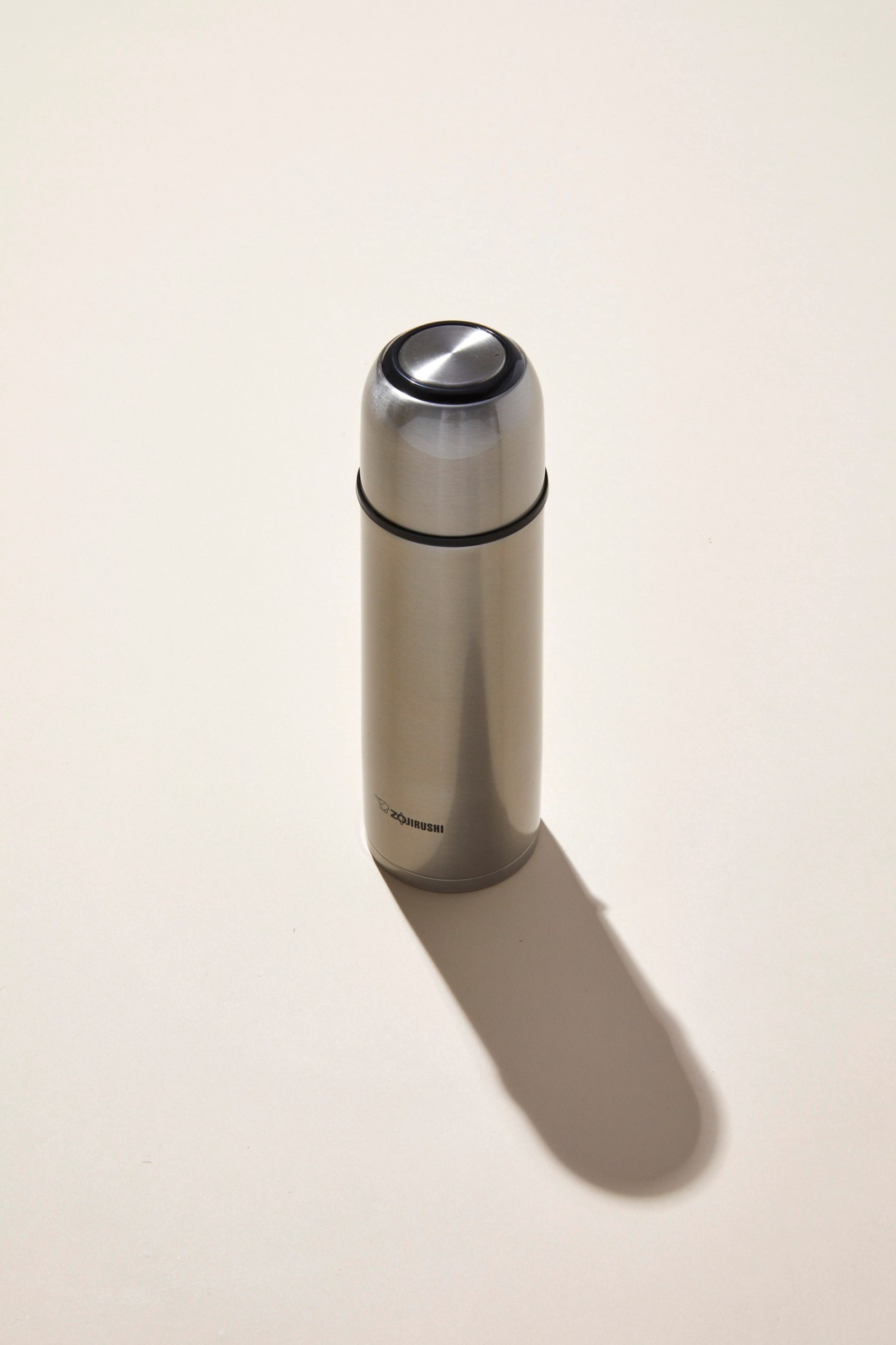 A sleek stainless steel thermos flask with black accents and cap, casting a shadow on a light background