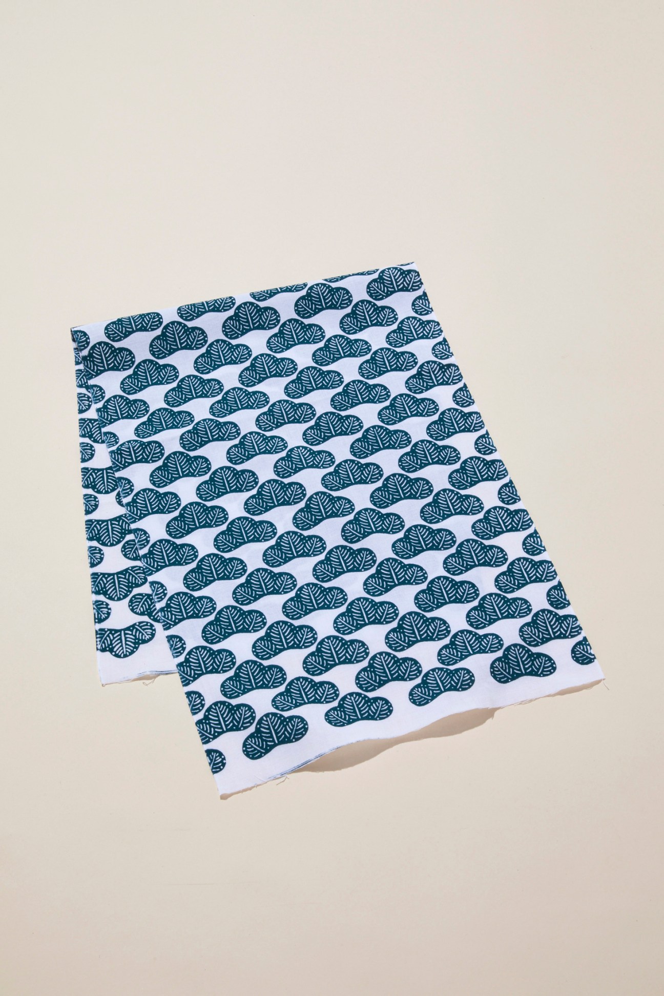 Two white fabric napkins with repeating dark blue tree pattern laid on beige surface