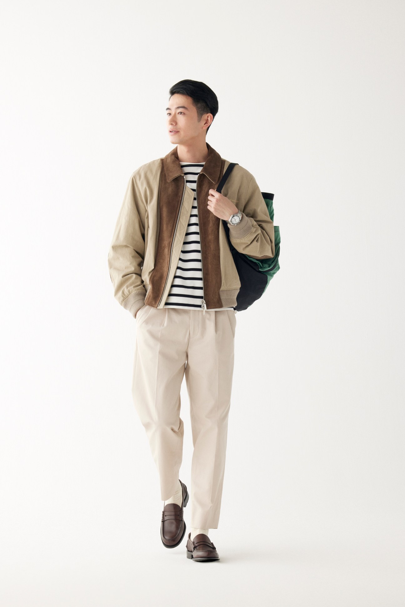 Man wearing lightweight jacket over striped t-shirt with tailored trousers and leather shoes, holding backpack