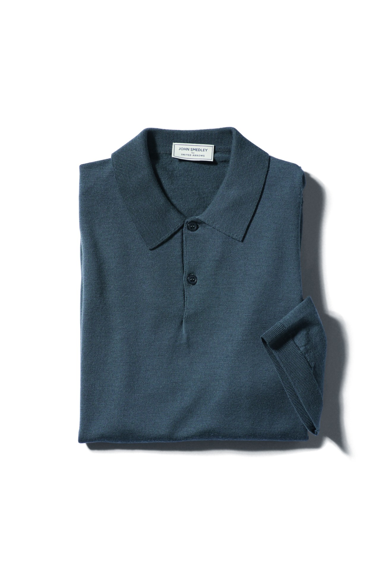 Dark teal knitted polo shirt by John Smedley for United Arrows folded and displayed on white background