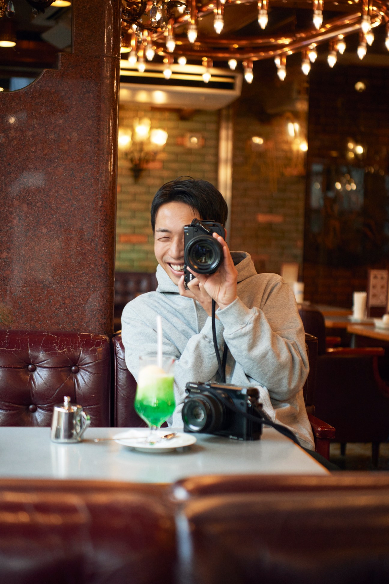Kentaro Ito holding camera in cafe with warm lighting and additional camera equipment on table