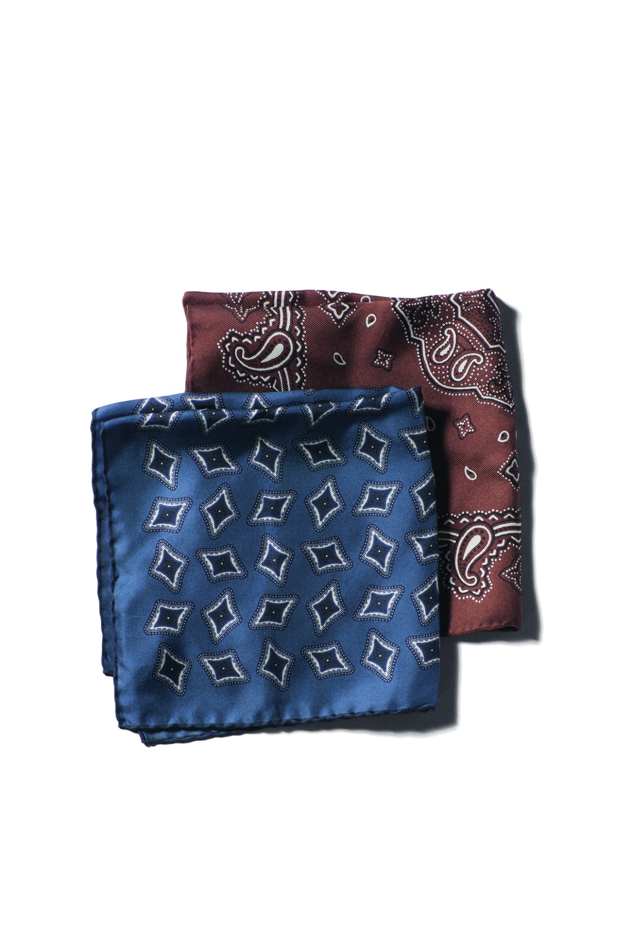 Two folded pocket squares with paisley patterns, one blue with diamond motifs and one burgundy with paisley designs