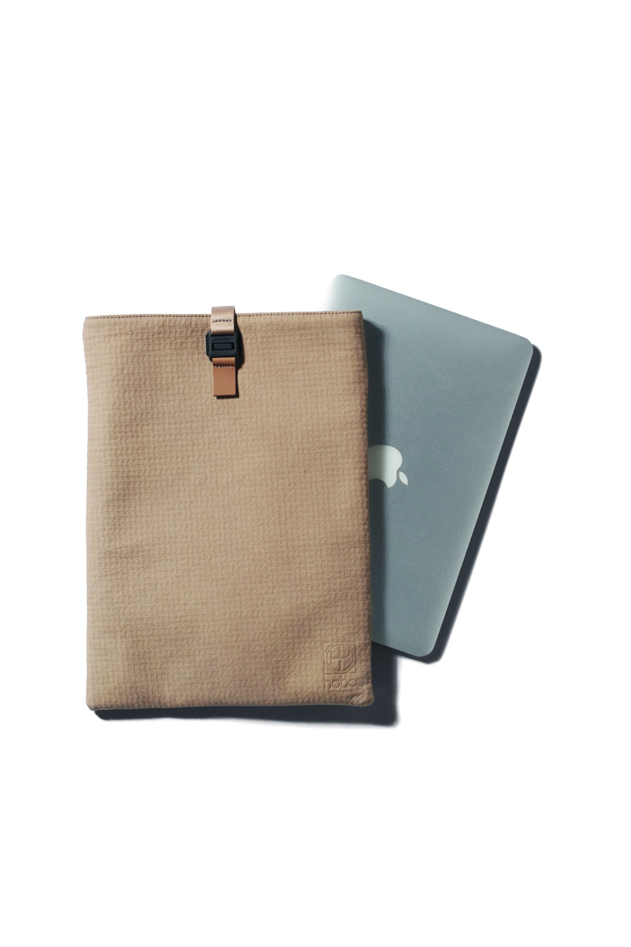 Woven beige laptop sleeve with leather strap closure next to gray MacBook on white background