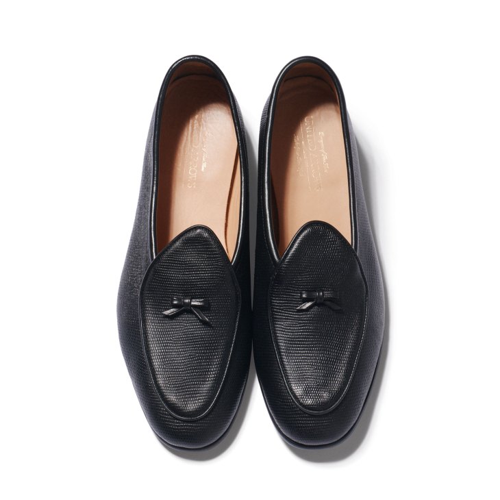 Black textured leather loafers with small bow details and tan leather lining photographed from above