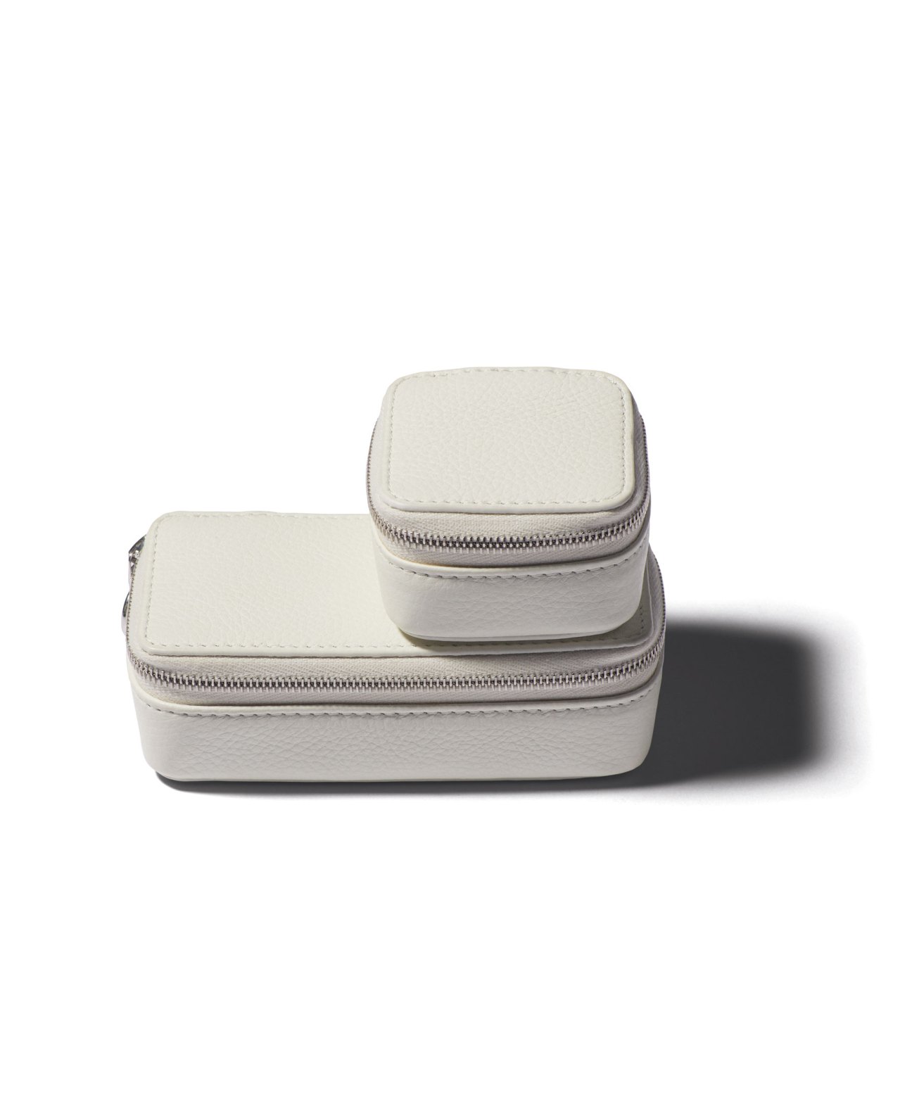 Two cream-colored leather accessory cases with zippers stacked on top of each other