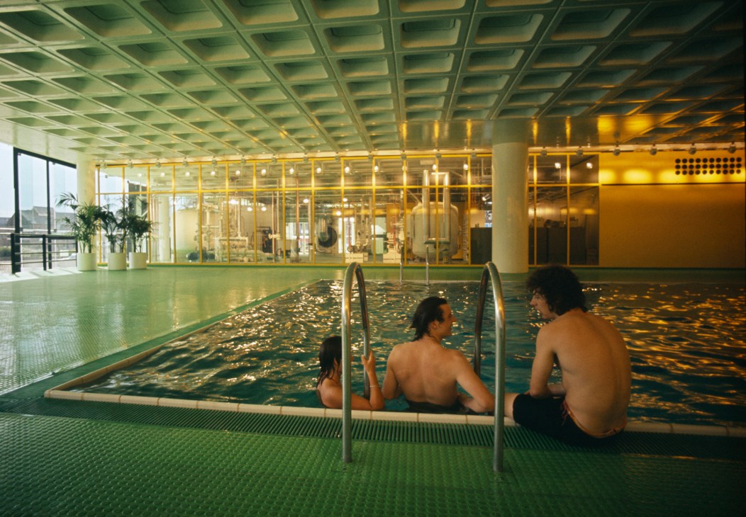 Interior of Willis Faber & Dumas office pool with three people in the water under geometric ceiling grid, Ipswich, 1975.