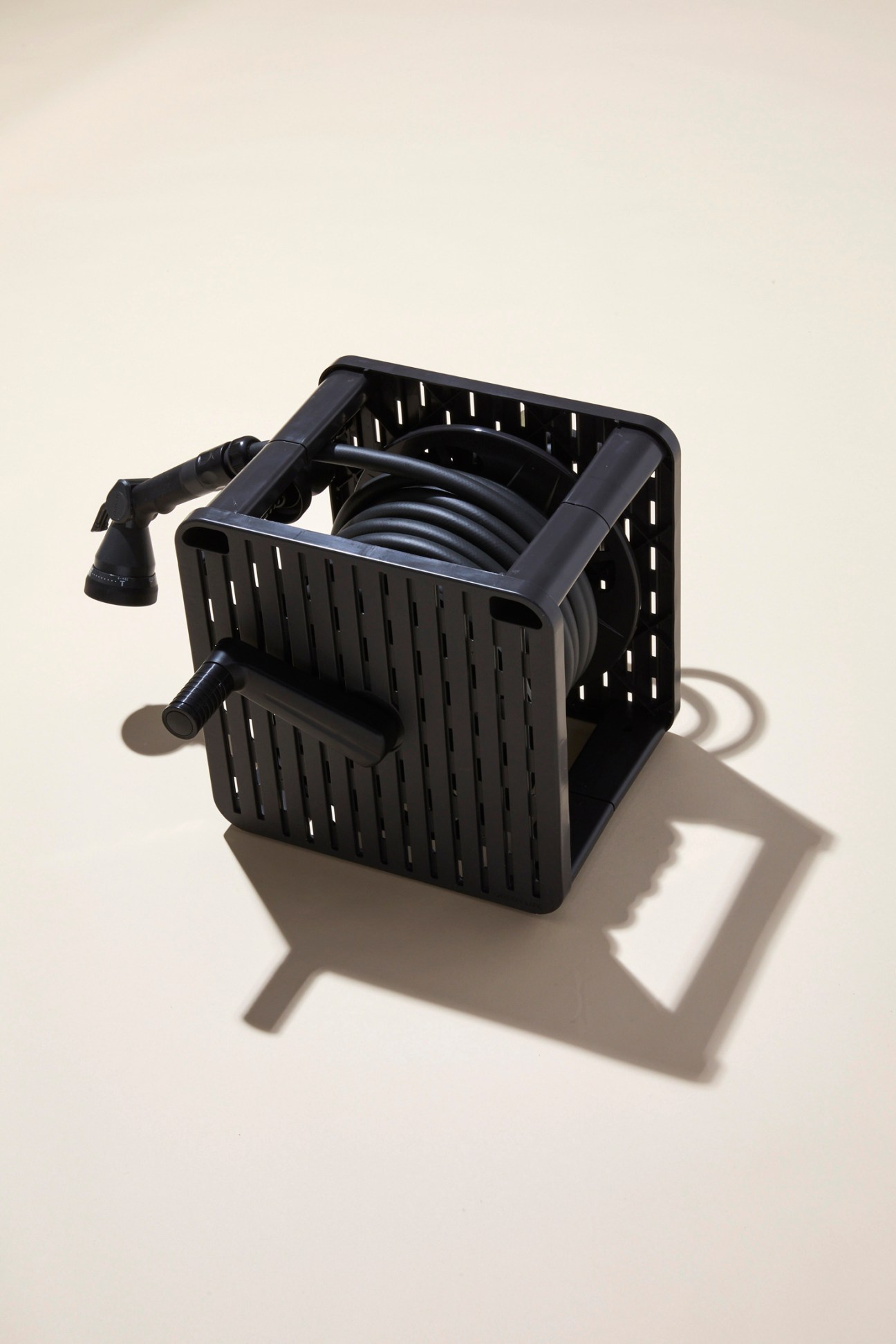 Black plastic garden hose storage crate with coiled hose and spray nozzle against neutral background