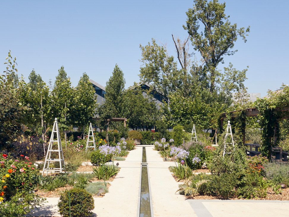 Formal garden with concrete pathways, water channel, white trellises, and diverse plantings at Davines Village