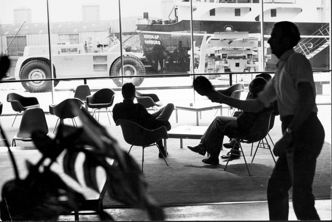 People sitting in modern chairs in a bright office lounge with large windows overlooking Fred Olsen's 1970 Isle of Dogs building and harbor.