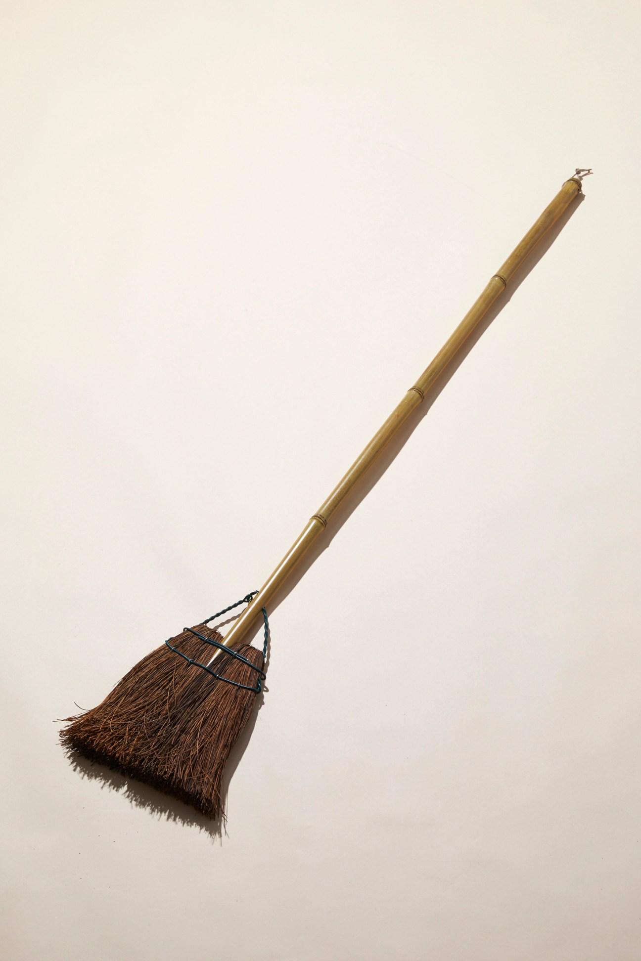 Traditional Japanese bamboo broom with natural bristles and wire binding against neutral background