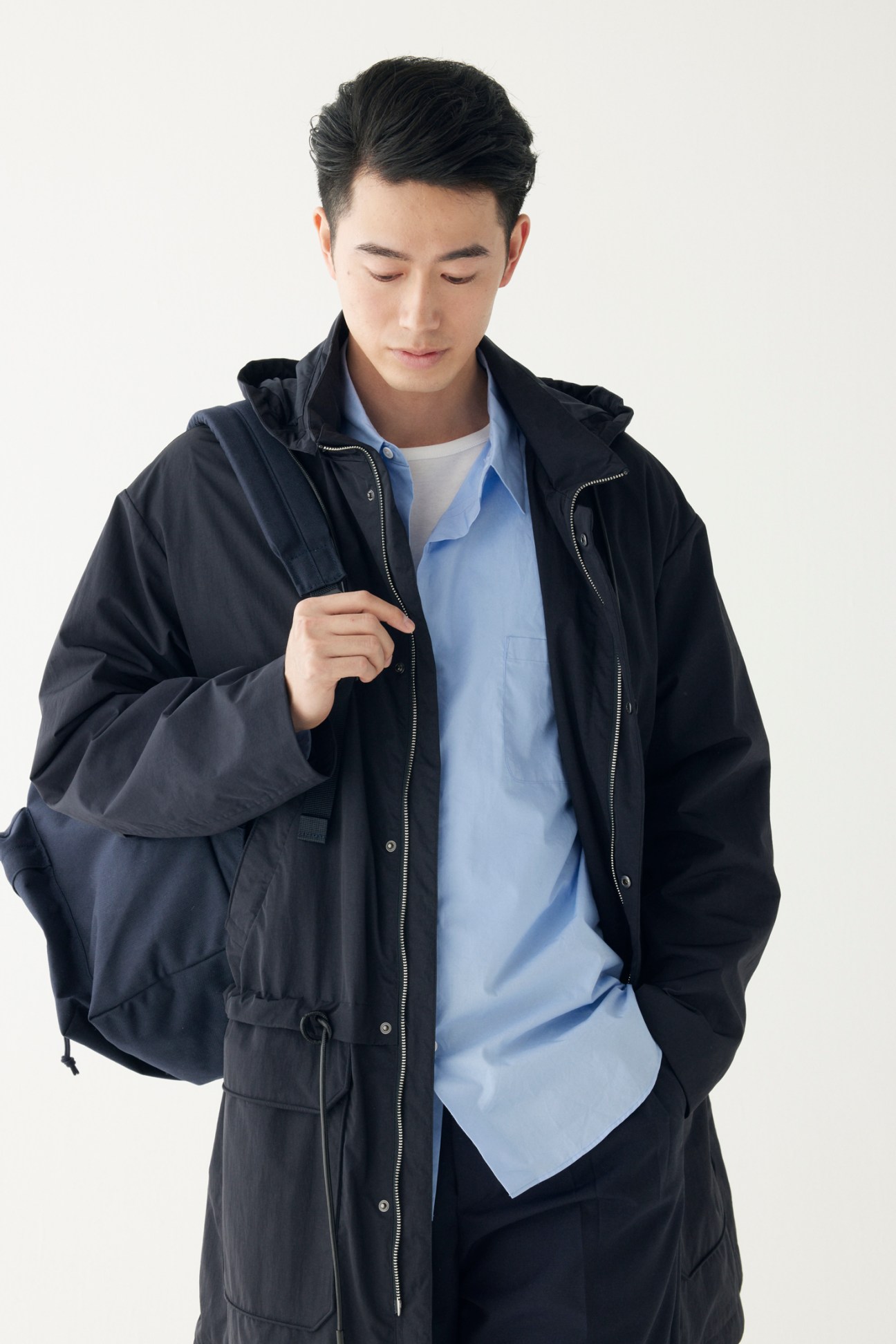 Man wearing dark navy coat over light blue shirt with white t-shirt, looking down