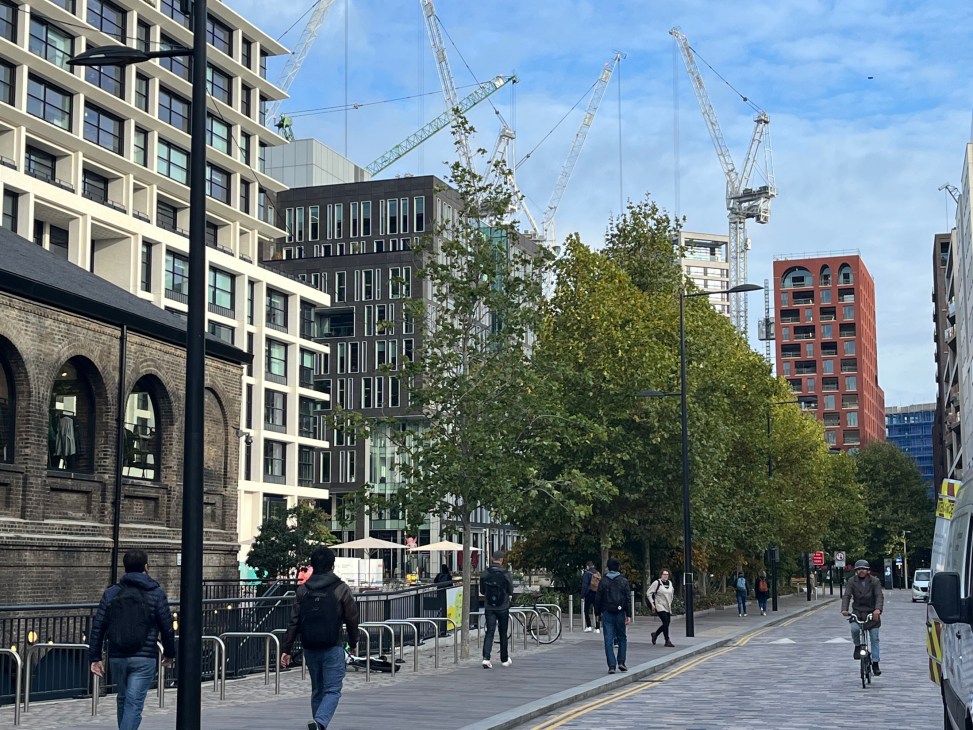 King's Cross development with modern buildings, construction cranes, and pedestrians walking on a paved street