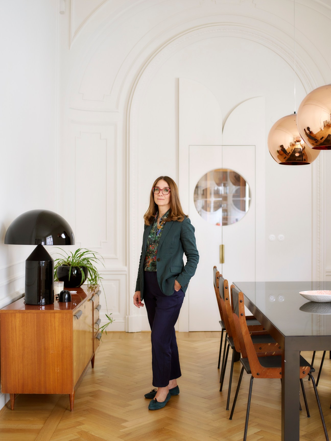 Woman in green blazer standing in modern interior with arched white walls and copper pendant lights
