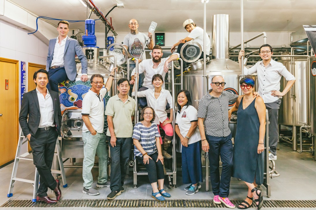 Team of Moonzen craft beer brewery staff posing together in their Hong Kong facility with brewing equipment.