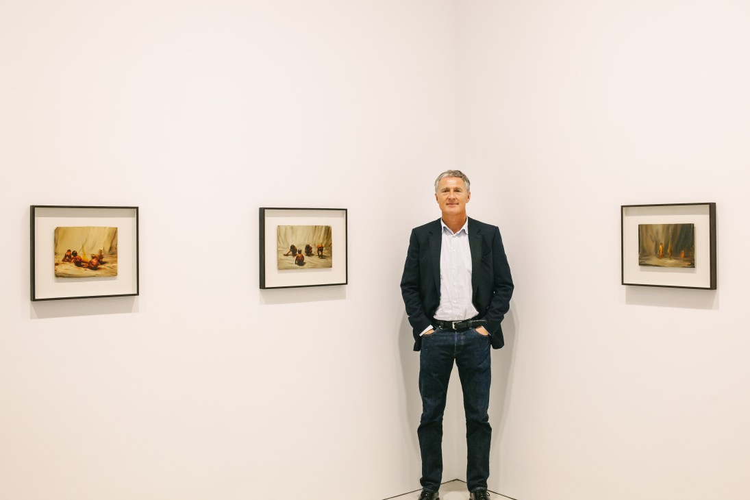 David Zwirner standing in a gallery space with framed artworks on white walls.