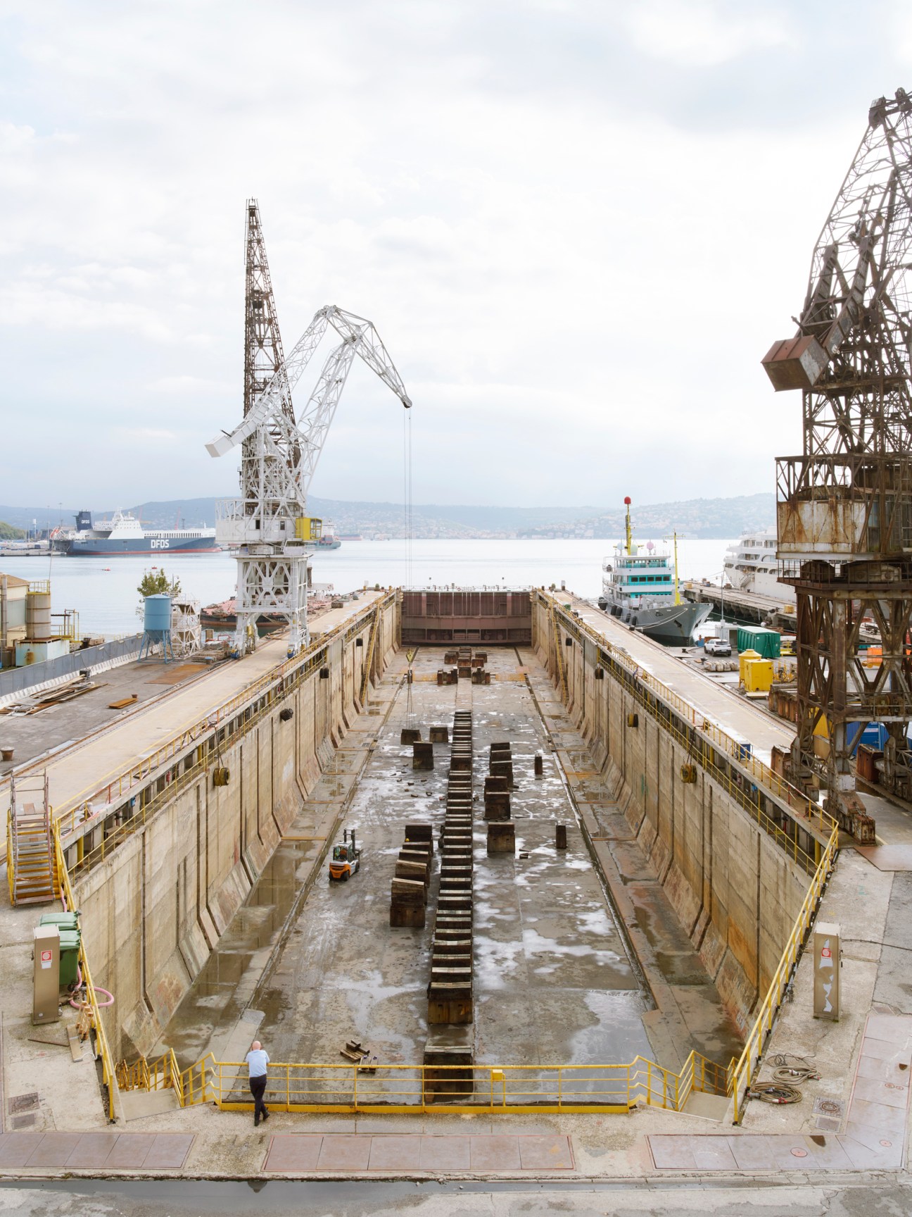 Large empty dry dock at Trieste port with concrete walls and cranes visible