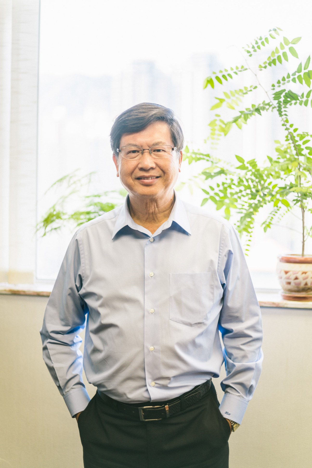 Program managing director Leo Leung stands smiling in an office with potted ferns behind him.