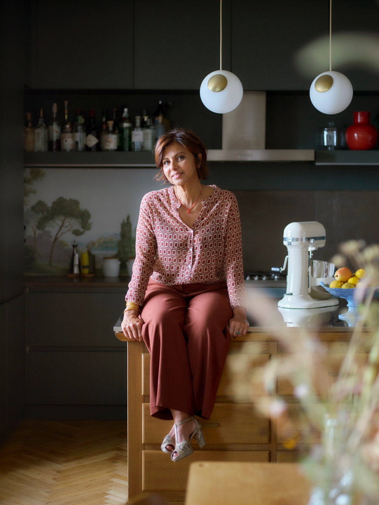 Woman sitting at kitchen counter in modern interior with pendant lights and shelving