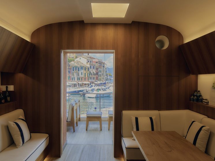 Curved wood-paneled interior of yacht or boat cabin with beige seating and view to Mediterranean coastal town