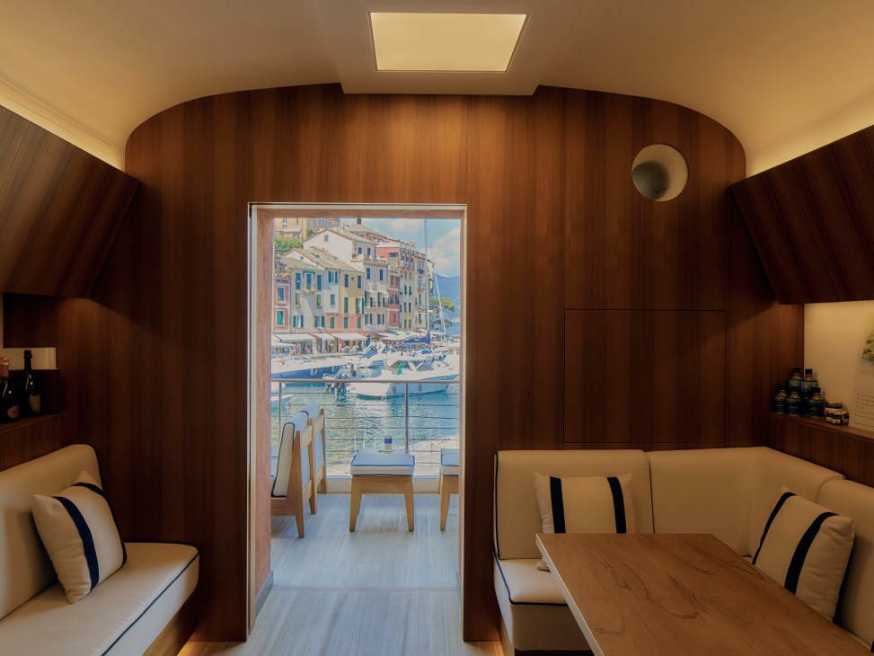 Curved wood-paneled interior of yacht or boat cabin with beige seating and view to Mediterranean coastal town