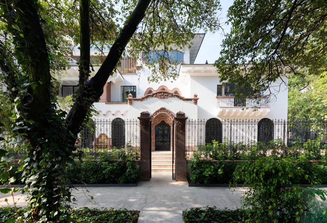 White 1940s mansion Casa Polanco in Mexico City with ornate terracotta gate framed by tree branches.