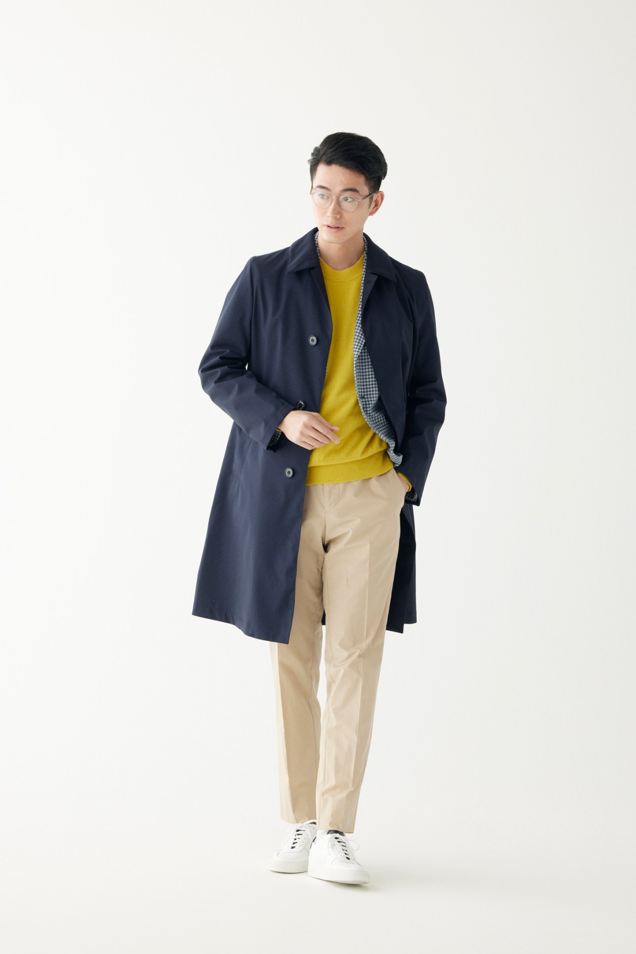 Man wearing long coat over layered casual outfit with trainers and glasses