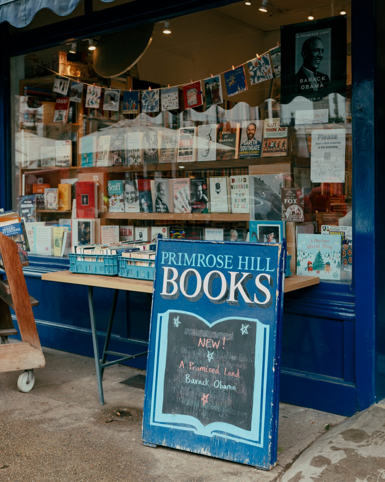 Storefront of Primrose Hill Books with blue signage, book displays in window, and chalkboard sign advertising new releases