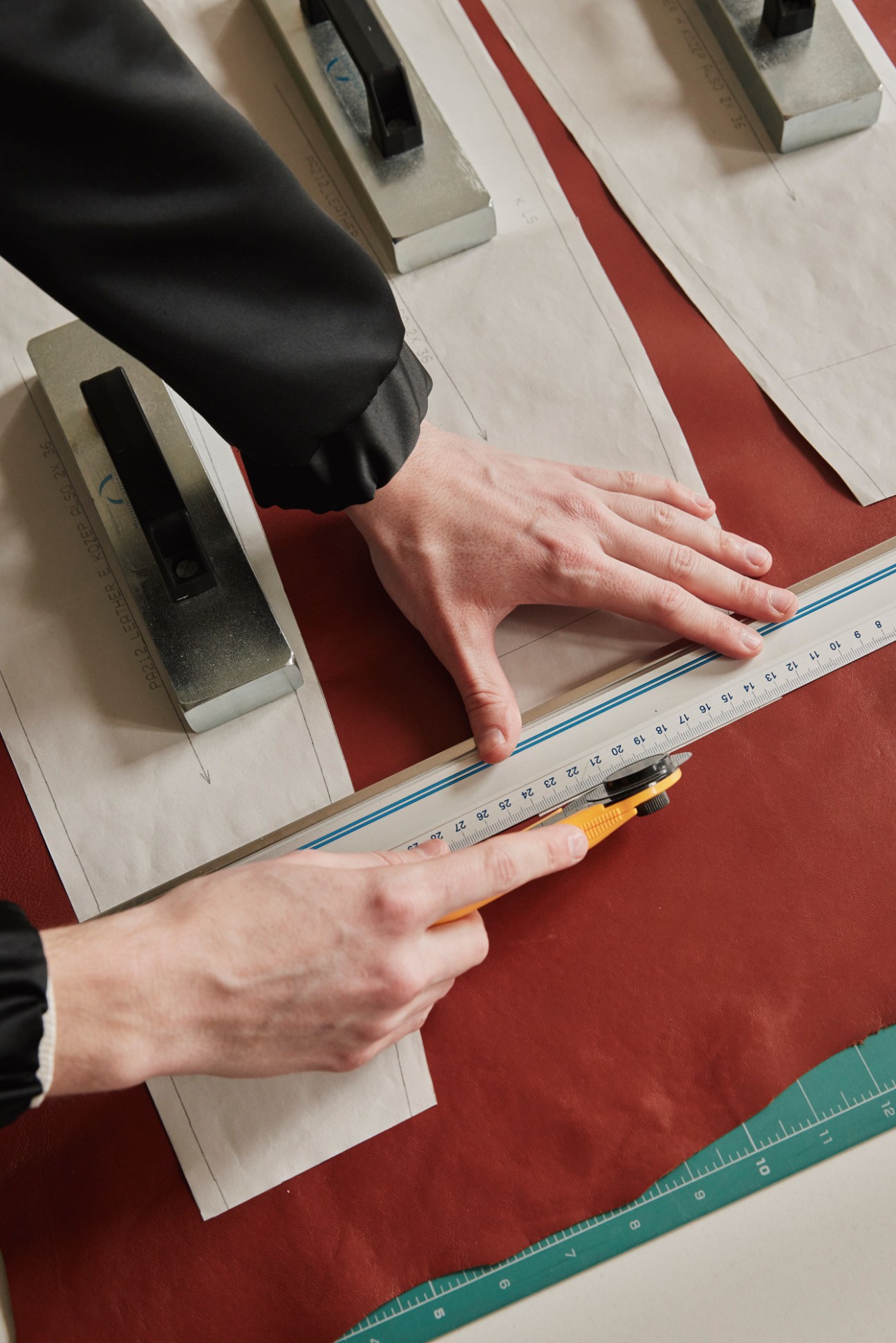 Hands using a ruler to measure and cut fabric patterns on a cutting table