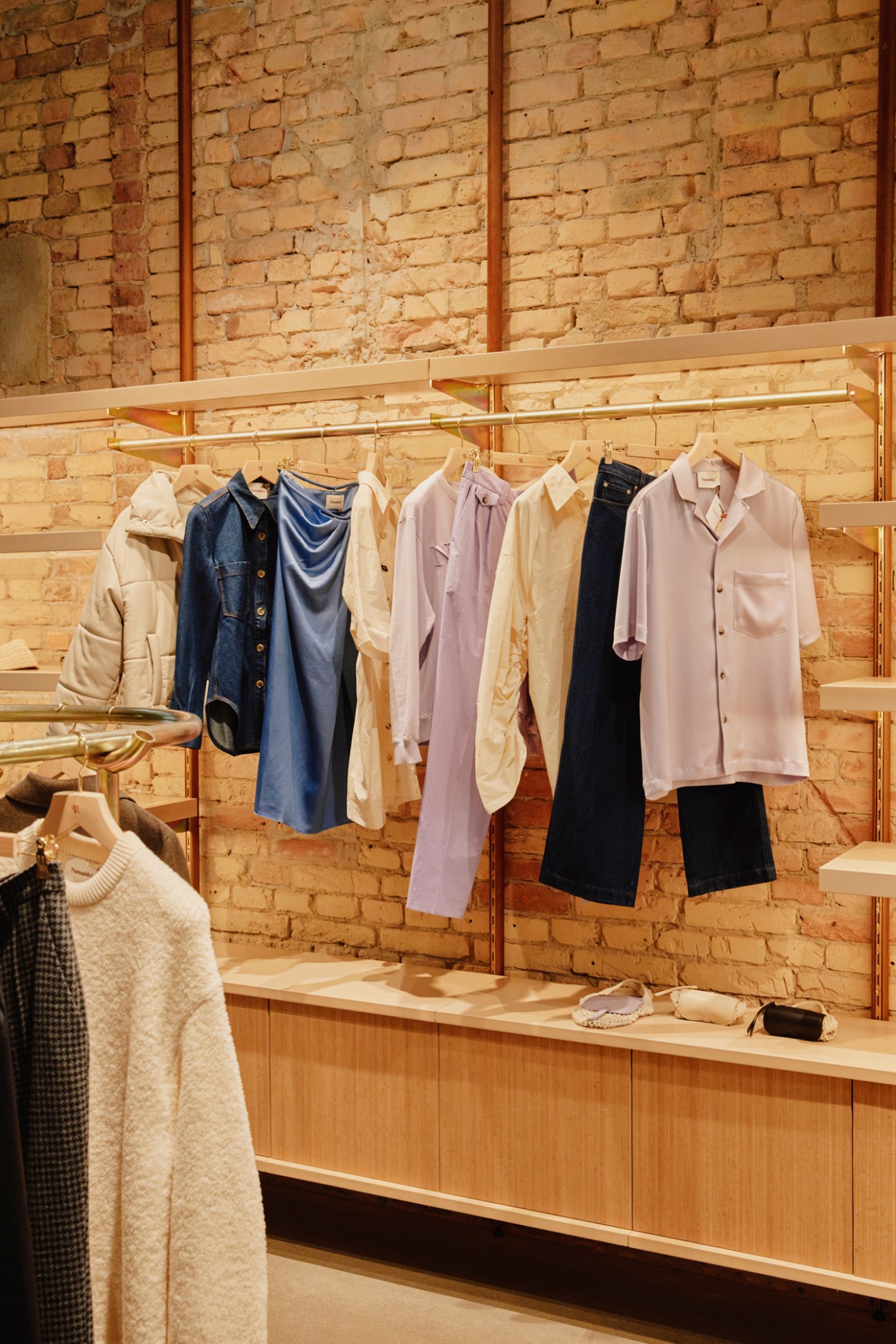 Clothing rack with neutral-colored garments hanging against exposed brick wall in modern retail space