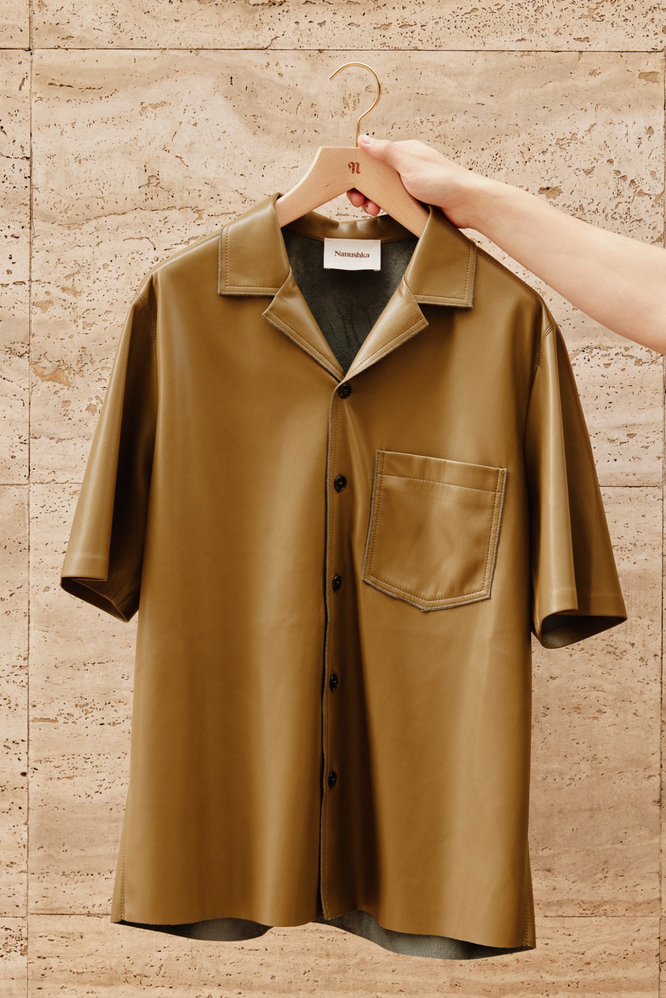 Olive green button-up shirt hanging on wooden hanger against textured concrete wall